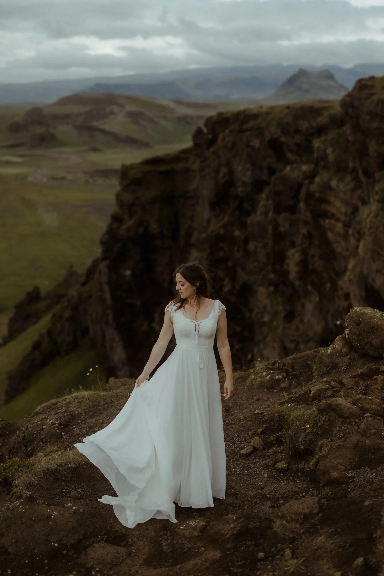 Braut im weißen Kleid vor einer isländischen Berglandschaft.